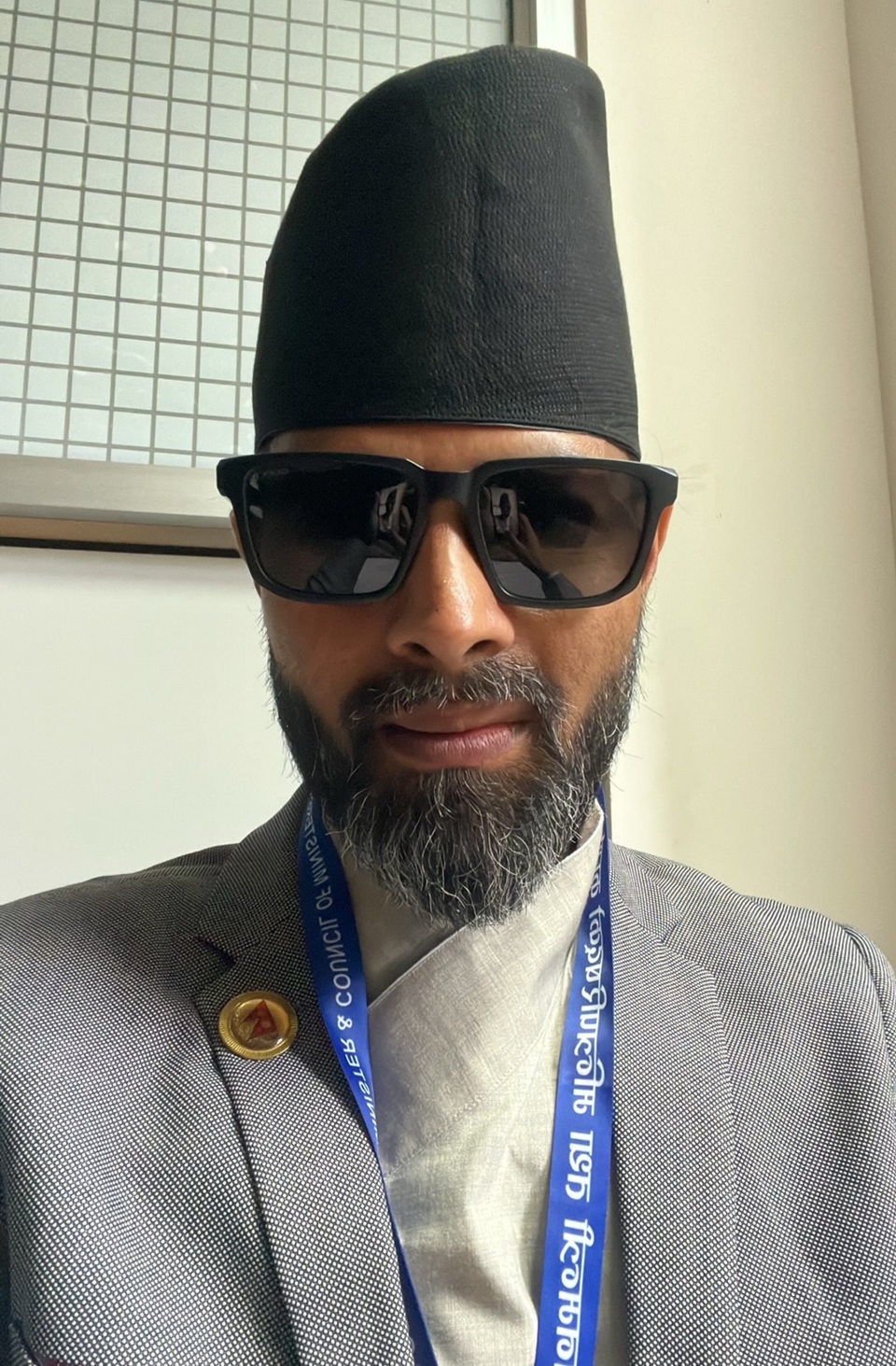 Padam Sundar Kafle in a black Nepali topi, dark sunglasses and a grey blazer over a daura